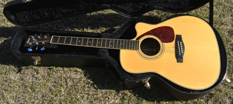 This is a picture of an acoustic guitar resting in its case, which is sitting open on a grassy area. 