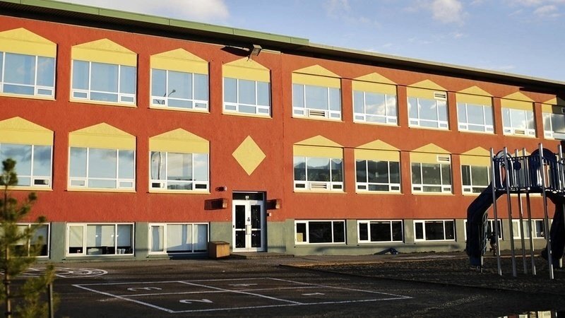 This is a picture of the front of a school building. This red brick building has many large windows in the front of it. 