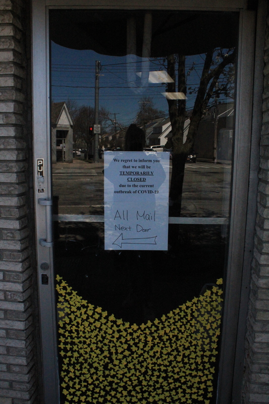 Two signs on a business door that says "We regret to inform you that we will be temporarily closed due to the current outbreak of COVID-19" and "All mail next door (with an arrow pointing left)."