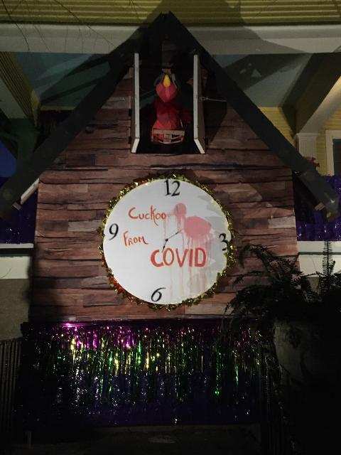 House decorated for Mardi Gras.  A white cardboard clock has a pink flamingo in the center and text which reads, "Cuckoo From Covid". 