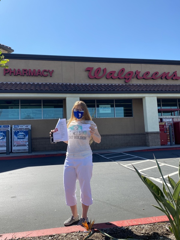 This is a picture of a woman standing in front of a Walgreens pharmacy holding her new vaccine card after receiving her first COVID-19 vaccine shot.  