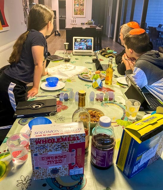 Three people at a table set up for Pesach staring at a computer. 