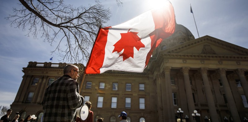 This is a picture taken of a man flying a Canadian flag upside down in front of a government building. 
