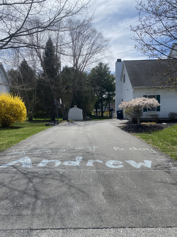 Chalk writing on a driveway by a basketball hoop. 