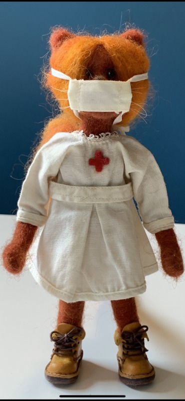 A cat doll that is dressed as a nurse and wearing a face mask. 