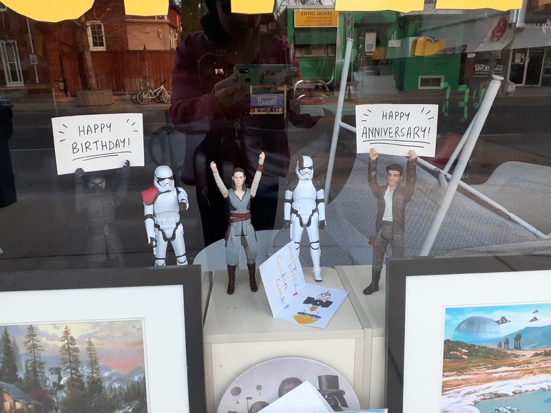 This is a picture of four Star Wars action figures posed standing in a window, holding signs reading "Happy Anniversary!" and "Happy Birthday!". 