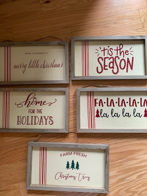 Five wooden signs reading Have Yourself a Merry Little Christmas, Tis the Season, Home for the Holidays,  Fa La La La La La La La La, and Farm Fresh Christmas Trees. 