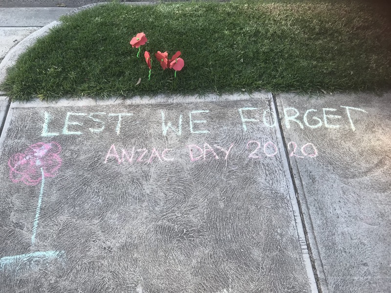 Chalk writing on a sidewalk that reads "Lest We Forget ANZAC Day 2020". 