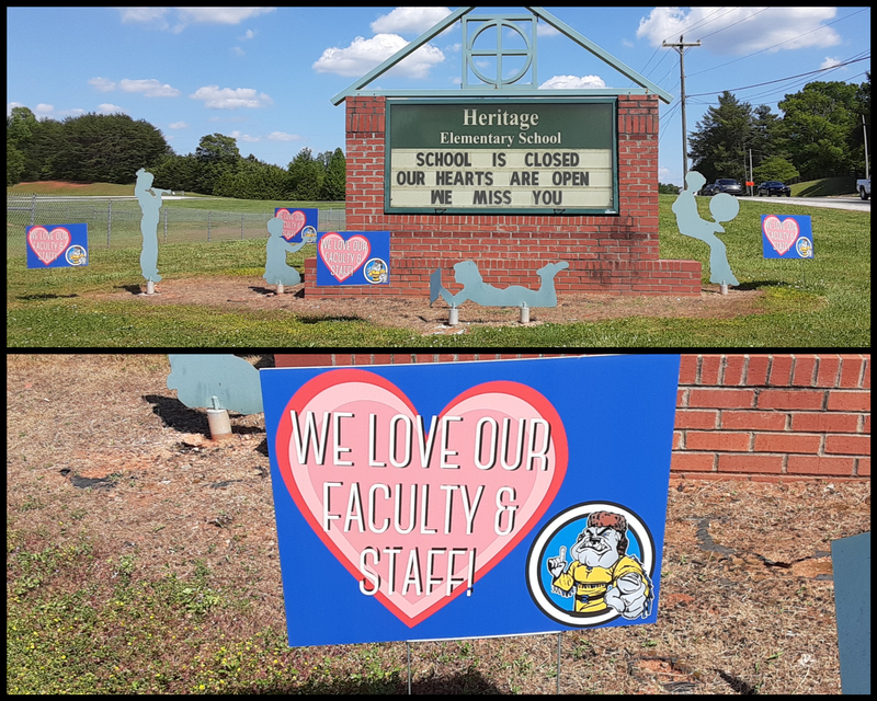 A brick sign outside of Heritage Elementary School stating, "School is closed. Our hearts are open. We miss you." Around the brick sign are eight smaller signs. Four of them have the words "We love our faculty and staff" surrounded by a pink heart. The other four signs are silhouettes of children.