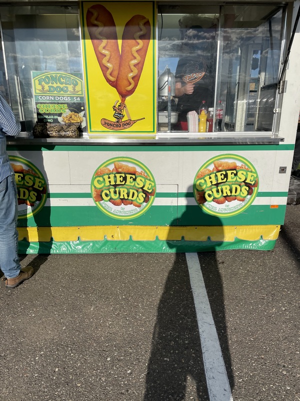 This is a picture taken of a colorful green and yellow corn dog stand that also sells cheese curds, per an advertisement on the front. 