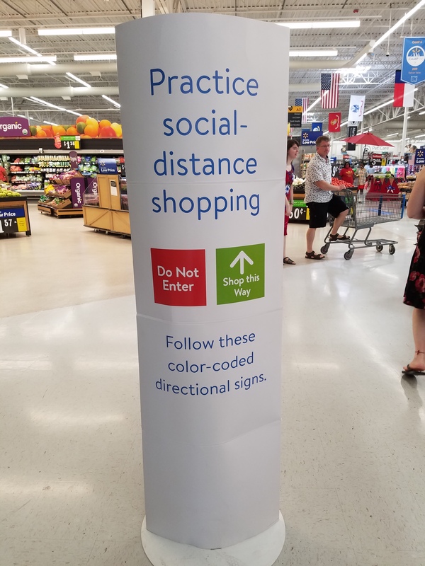 This is a picture of a sign at a store which reads "Practice social-distance shopping", with a red and green sign below reading "do not enter" and "shop this way" respectively. Below these signs, a message reads: "follow these color-coded directional signs". 