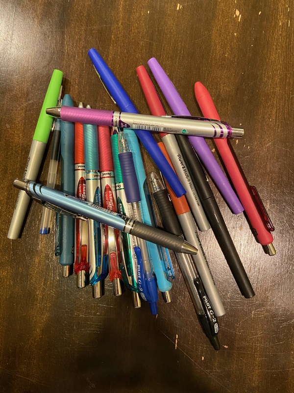 This is a picture of an assortment of pens and pencils set on top of a desk. 