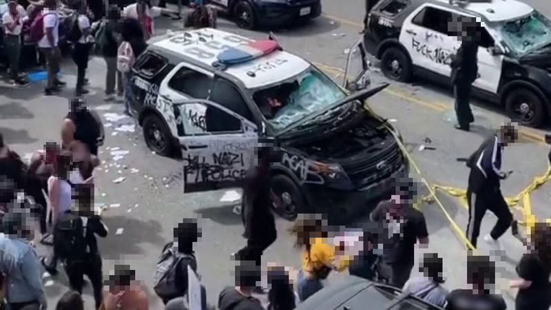 A picture of a group of people surrounding two destroyed police vehicles during the Black Lives Matter protests. 