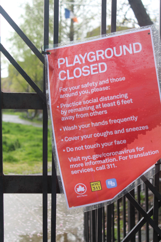 A red and white sign on a gate warning that a playground is closed. 
