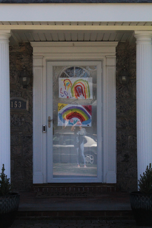 A residential house with two rainbow drawings on the front screen door.