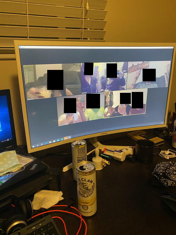 This is a picture of a computer monitor which has a zoom call open on it. Each person is offering a toast with their drink, but their faces are blurred out.