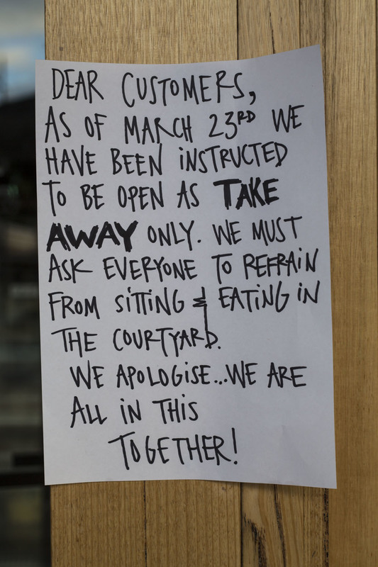 A piece of paper is taped up on a wooden door telling patrons that their store will be take out only and to refrain from sitting or eating in the courtyard. 