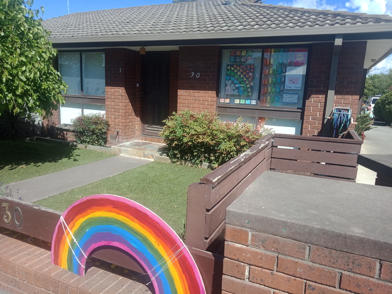 Picture of a home with windows and a fence decorated with rainbow patterns. 