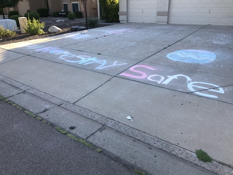 The words "Stay home, stay safe" are written with chalk on a driveway. 