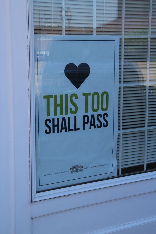 A sign in a window reading "This too shall pass".
