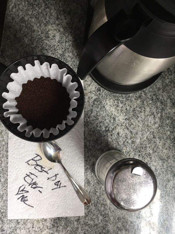 A coffee maker next to a sugar container and a coffee filter.