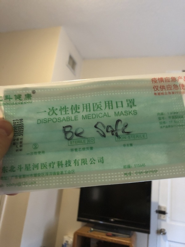 This is a picture of a disposable face mask with the words "be safe" written on it in black marker. 