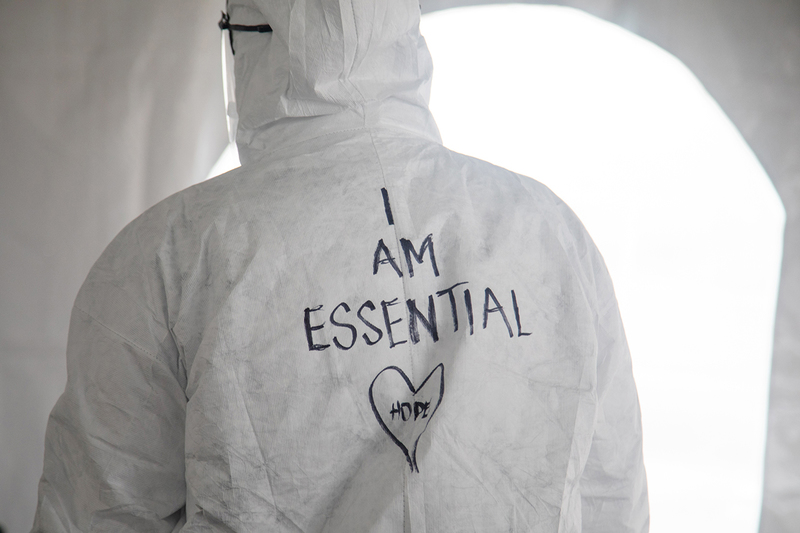 A photo of a person in a white hazmat suit with the words "I am essential" and "hope" written on the back.