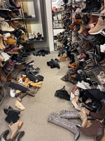 This is a picture taken of a messy footwear isle at a store. Shoes lie strewn across the ground of the isle. 