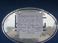 A paper sign reading "Temporarily Closed due to Sedgwick County bar shutdown order. Hopefully see you Aug 22nd".  