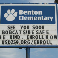 A Elementary school sign reading "See you soon Bobcats! Be safe. Be kind. Enroll now. USD259.org/enroll".