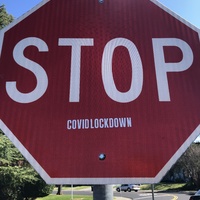 This is a picture of a red stop sign which has a sticker on it reading "STOP... COVIDLOCKDOWN". 