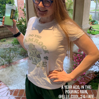 This is a picture taken of a girl smiling and holding a shamrock shake from McDonald's. She is wearing a white shirt, sweatpants, and glasses while rain can be seen falling in the background. A caption at the bottom of the photo reads: "A year ago in the pouring rain, @ellie_cool_j and I ate a feast of McDonald's and shamrock shakes in what we dubbed 'the end of the world as we know it' lunch, not realizing two hours later it would be."