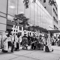 This is a picture of a group of doctors kneeling on the ground in solidarity with the Black Lives Matter movement. A large glass building is being them. 