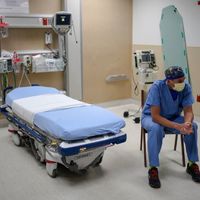 A photo of a healthcare worker sitting next to an empty hospital bed.