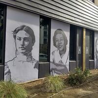 This is a picture taken of a series of murals that are painted on the side of a building. Various women in different periods of clothing are depicted in black and white. 