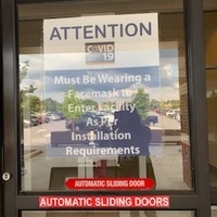 A picture of a sign posted on the door to the entrance to a military building at Fort Bragg, North Carolina which reads: "Attention! Must be wearing a face mask to enter facility as per installation requirements."
