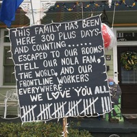 This is a picture taken of a sign in front of a person's house. The sign reads: "This family has been here 300 plus days and counting...... Escaped to our rooms. Tell our Nola fam, the world, and our front line workers everywhere...... WE LOVE YOU ALL!" 28 tally marks are drawn at the bottom of the sign. 