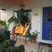 Front porch with Halloween decorations.  Two skeletons hold sign that says, "Six Feet When Possible, Y'all!".