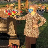 A photo of an older woman wearing a mask and standing by a grave.