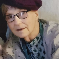 A woman is wearing a purple beret with black glasses on. She is wearing a white coat with a green shirt with diamonds on it.  