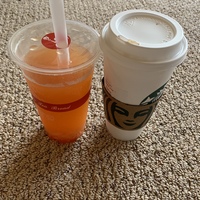 This is a picture of an orange drink set next to a Starbucks coffee cup. 