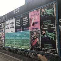 Two rows of posters for concerts on a black wall. 