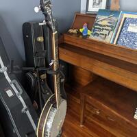 Banjo on a stand next to a wooden, upright piano.