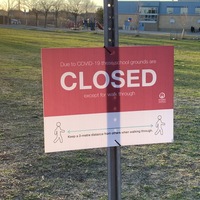Image of a sign in front of a school which reads due to Covid-19, these school grounds are closed except for walk-through.