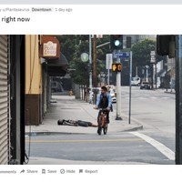 A screenshot of a picture of Downtown LA that shows a man riding a bike past another man who is wearing a mask and has collapsed on the street.