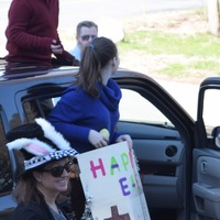 Adults and children around a black vehicle, a girl is holding a sign that says Happy Easter. 