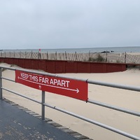 a red sign tied to a railing showing how far apart people need to stay