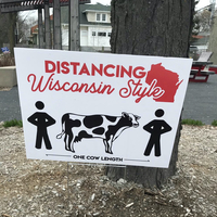 A sign that states "Social Distancing... Wisconsin Style: One Cow Length". 