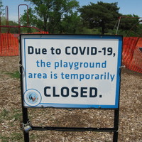 Playground in the background fenced off and sign in front with text, "DUE TO COVID-19, THE PLAYGROUND AREA IS TEMPORARILY CLOSED."