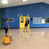 This is a picture taken of two women mopping a floor. 